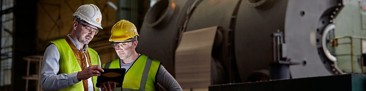 男工程师与工人正在黑暗的工厂中使用数字平板电脑。