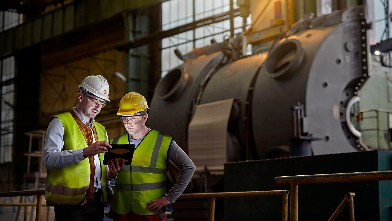 男工程师与工人正在黑暗的工厂中使用数字平板电脑。