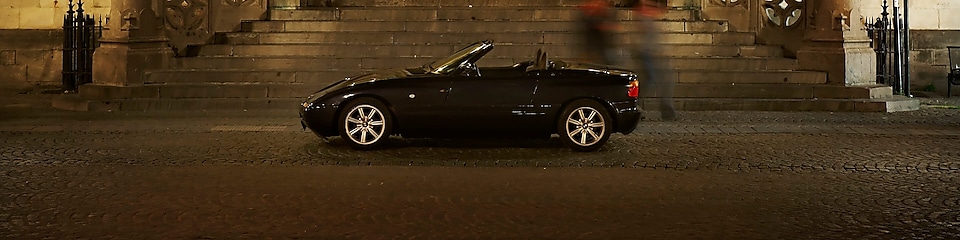 Black car parked outside of a large house at night, next to some stone steps