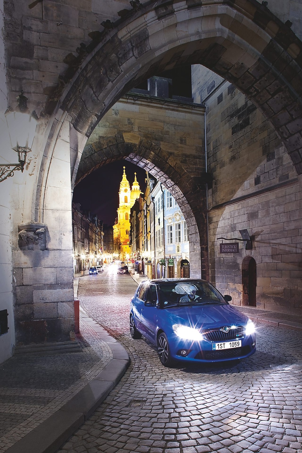 Blue car parked under an arch on a cobbled Prague road at night
