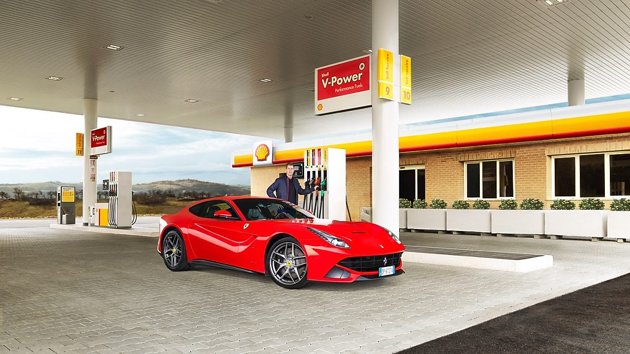 停靠在壳牌加油站前的红色法拉利以及斜倚在加油泵上的男士