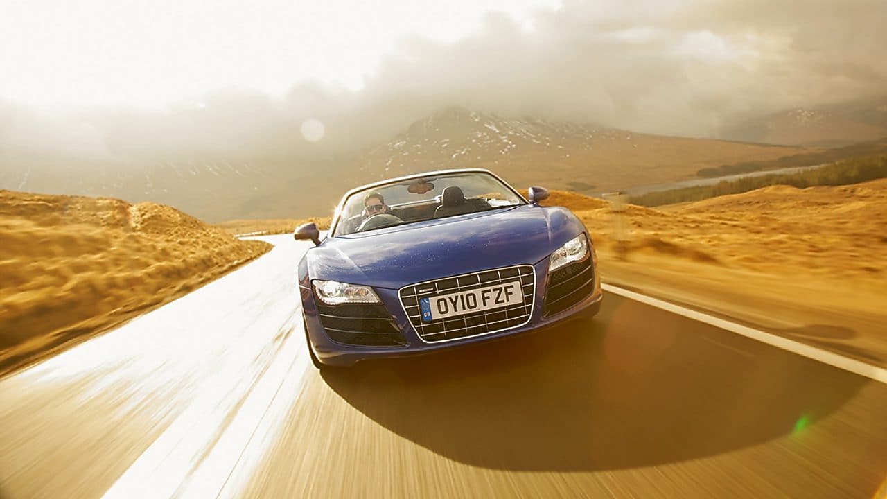 开启天窗的蓝色轿车,正面图,在被山地美景所环绕的乡间公路上行驶