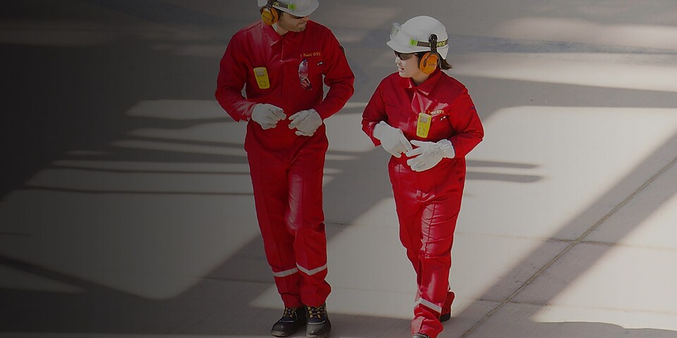 身穿红色工作服、头戴白色头盔和听力保护装置行走的男女工人