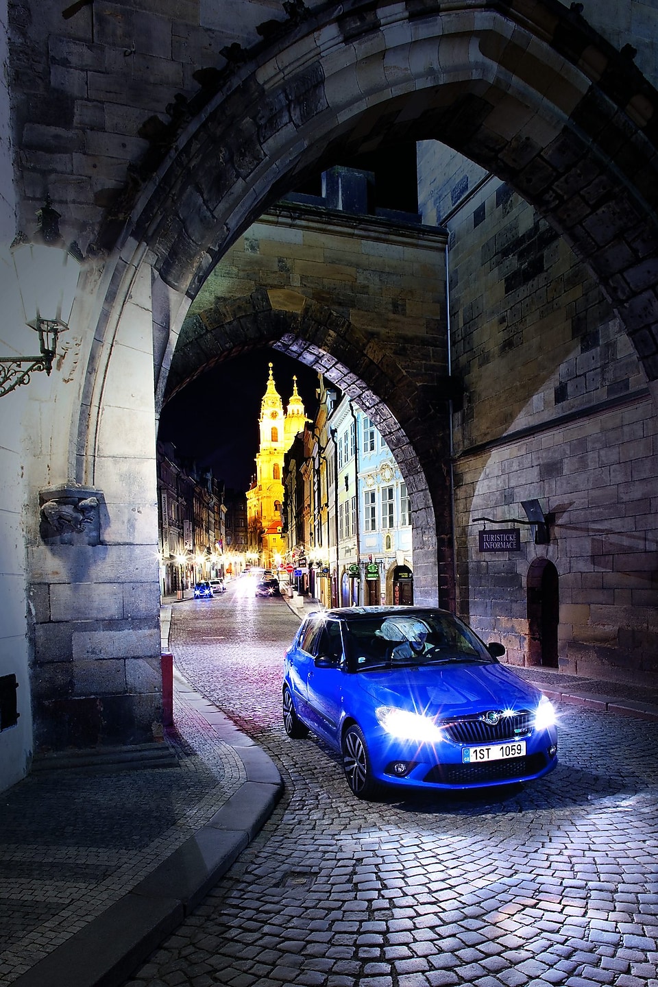 夜晚，在布拉格鹅卵石道路上的拱门下停靠的蓝色汽车